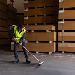 Portrait of young man with Down syndrome sweeping the floor, working in factory, warehouse. Concept of workers with disabilities, support in workplace.